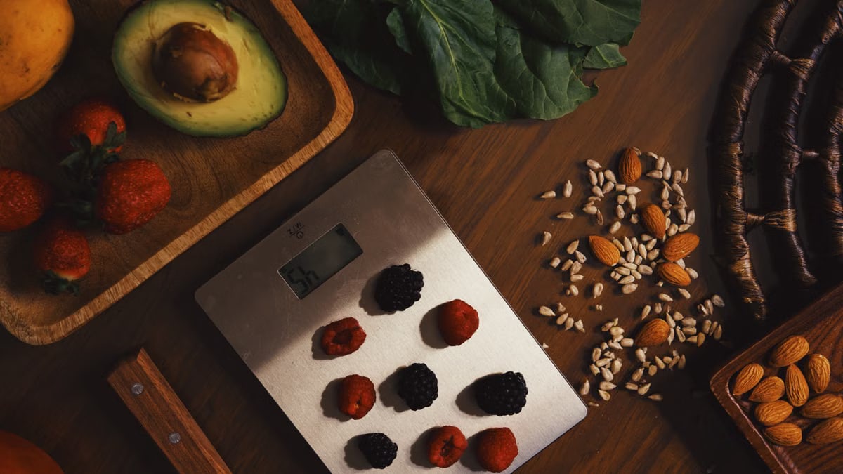 Top view of composed raw almond with seeds and avocado on table with berries on scales for cooking healthy dish